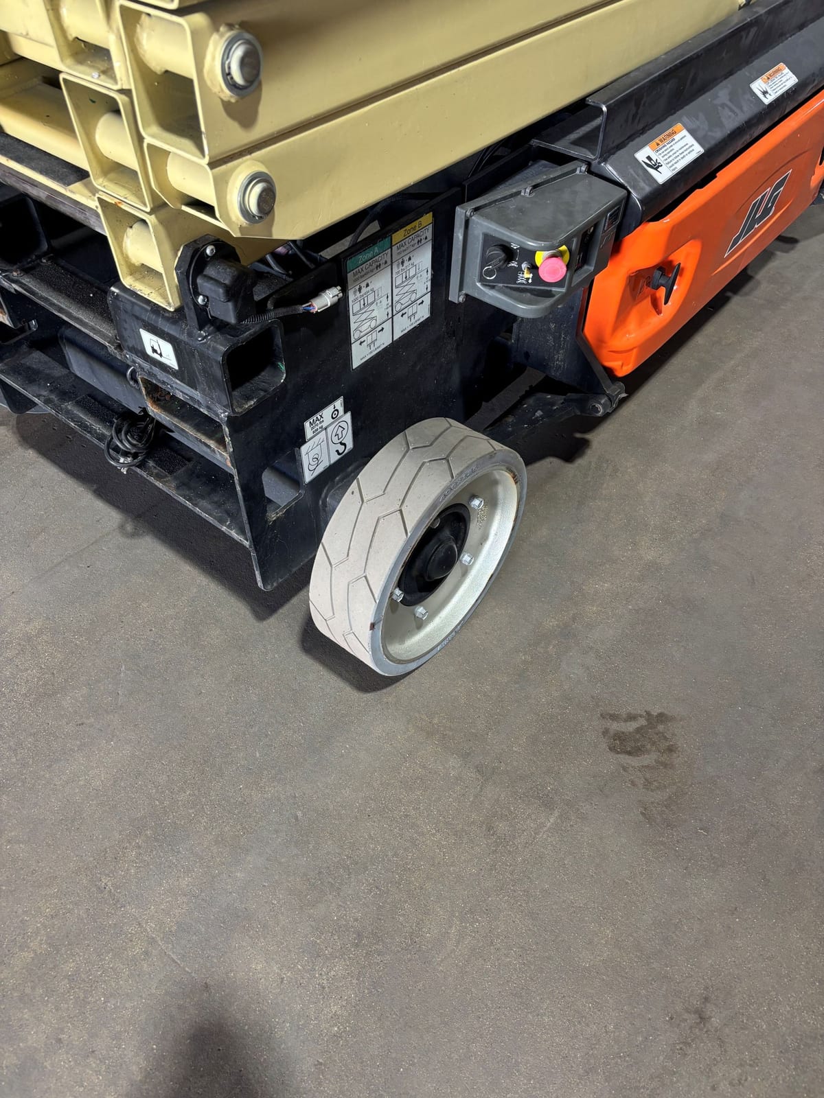 Chassis corner of the JLG 3246ES with the gray non-marking tire, ground control box, and platform capacity decals