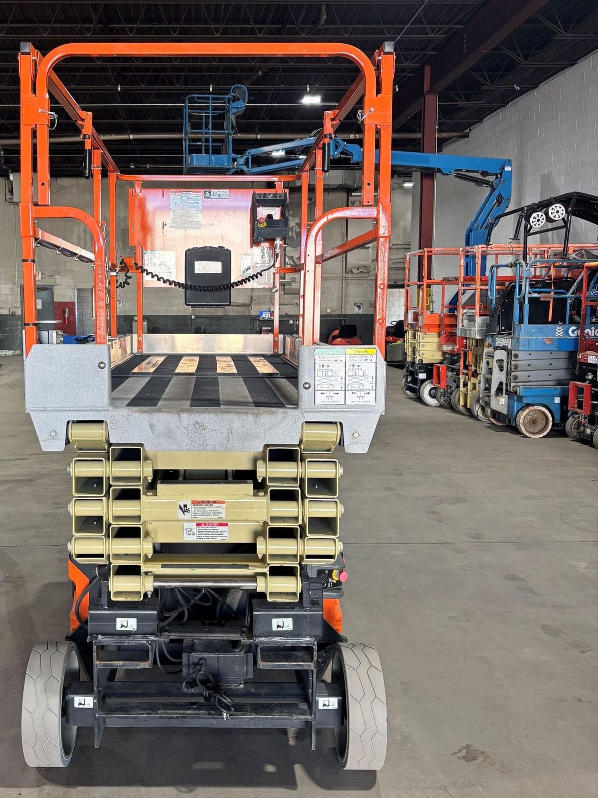 End view of a used 2014 JLG 3246ES electric scissor lift with the platform lowered, entry gate and stowed scissor stack facing the camera