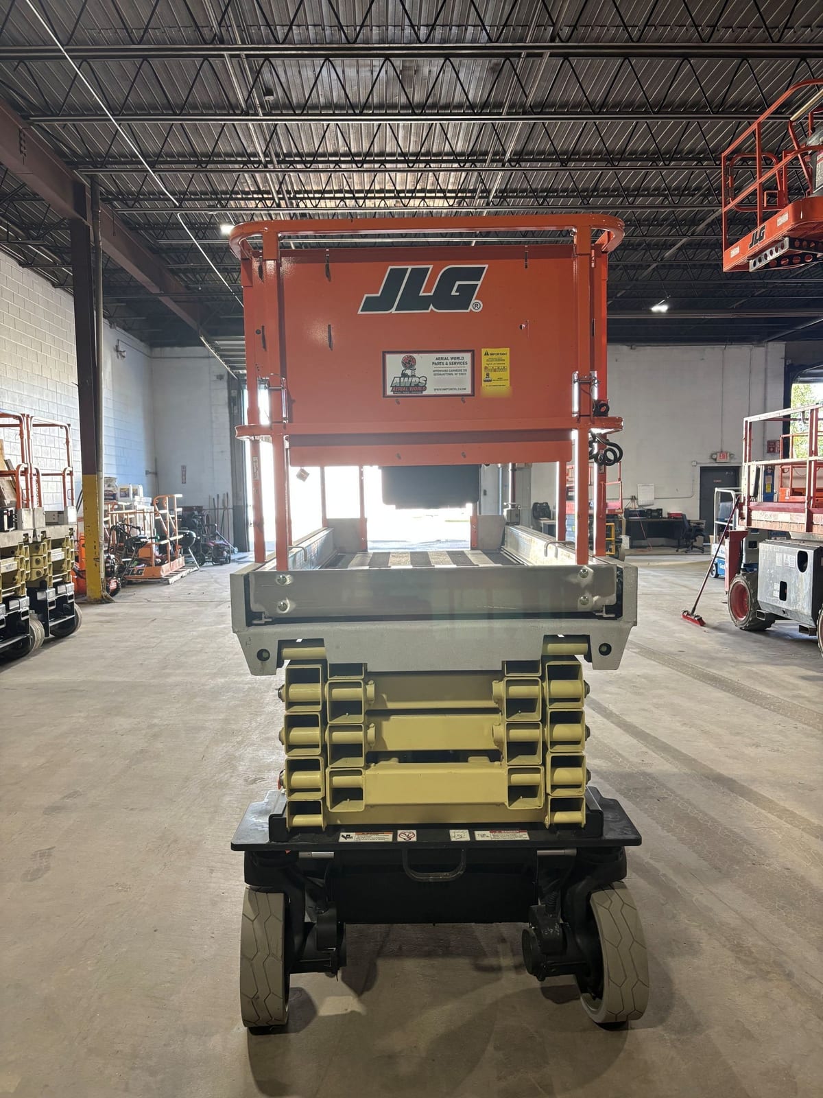 Gate end of the JLG 3246ES with the orange platform end panel above the stowed scissor stack