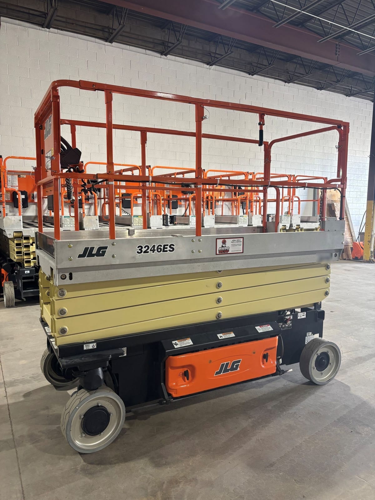 Side profile of a used 2014 JLG 3246ES electric scissor lift with the platform lowered, parked on the shop floor