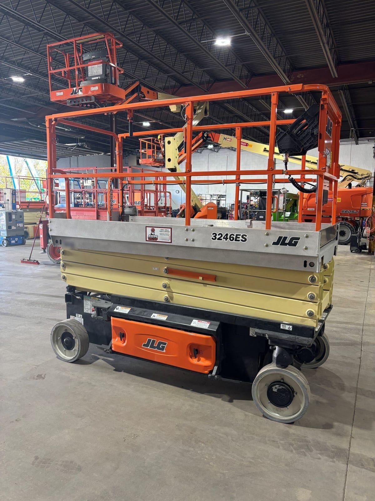 Opposite side of the JLG 3246ES showing the platform rails, the stowed scissor stack, and the orange battery tray cover
