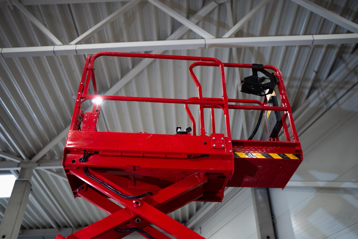 A red scissor lift extended toward a warehouse ceiling