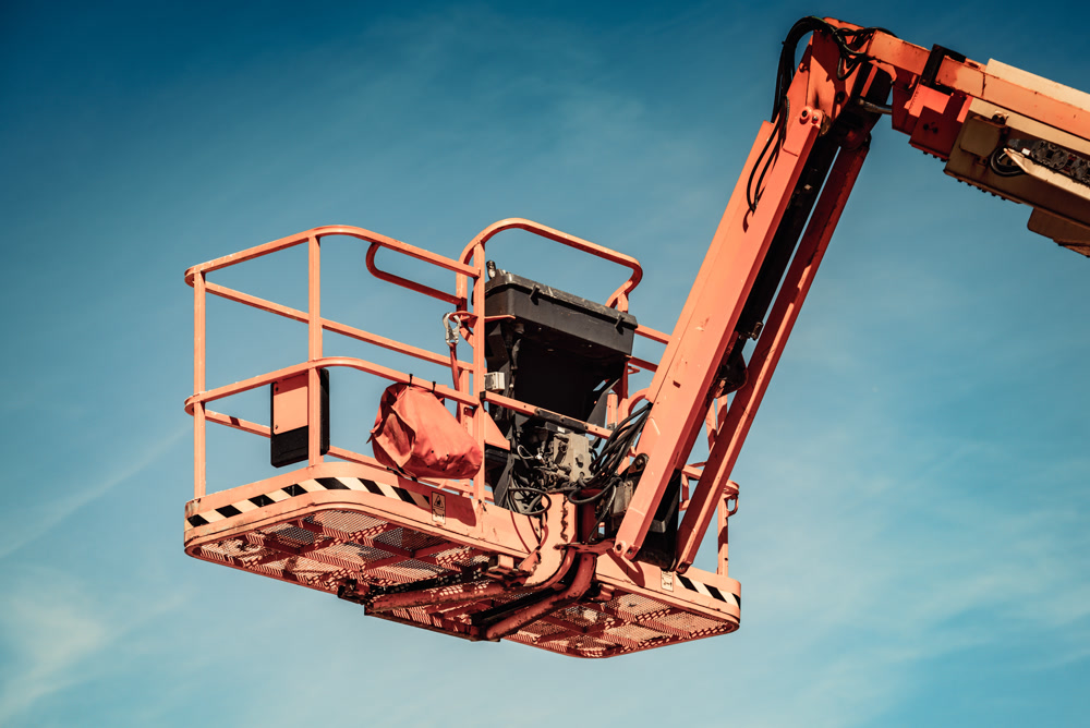 An orange boom lift basket raised against a clear sky