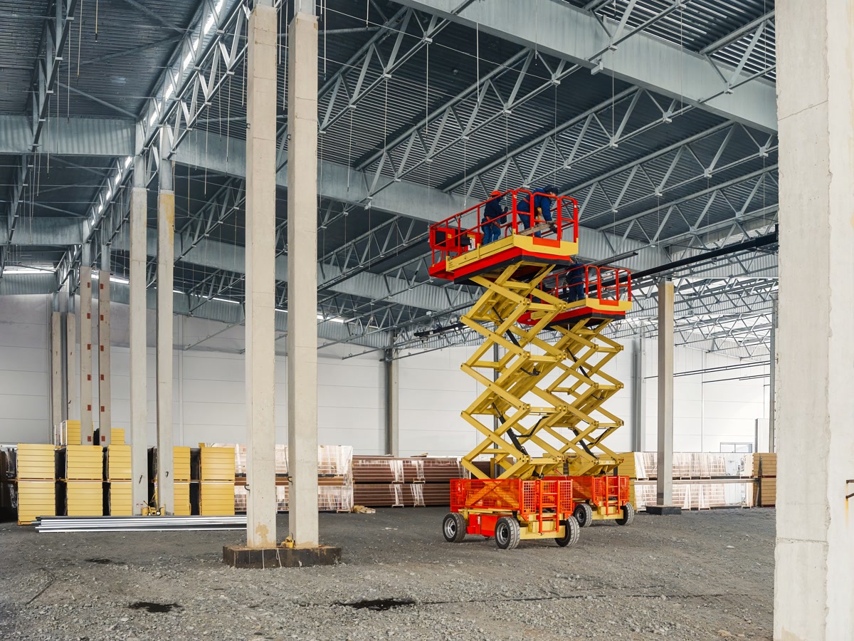 Scissor lifts raised inside a warehouse with workers at the rails